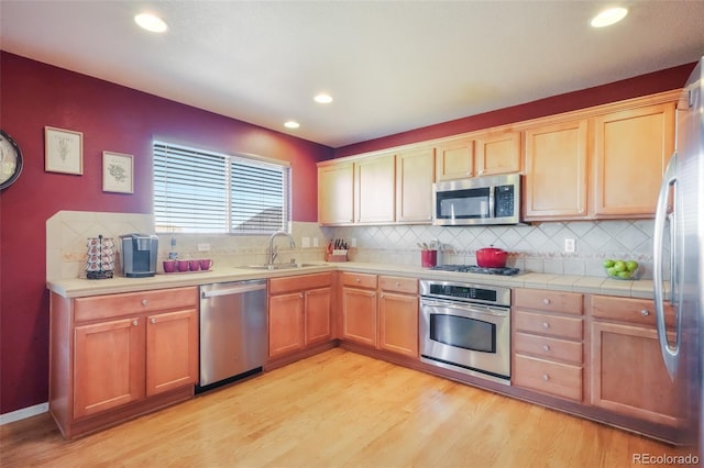 kitchen featuring tasteful backsplash, recessed lighting, appliances with stainless steel finishes, light wood-style floors, and a sink