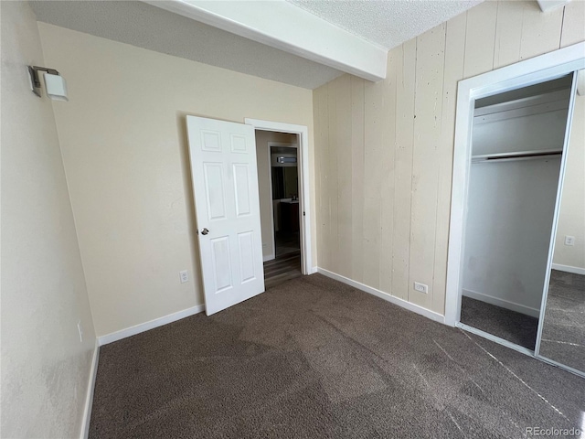 9995 E Harvard Ave Unit 261, Denver, CO 80231 - unfurnished bedroom featuring carpet flooring, beam ceiling, a closet, wooden walls, and a textured ceiling