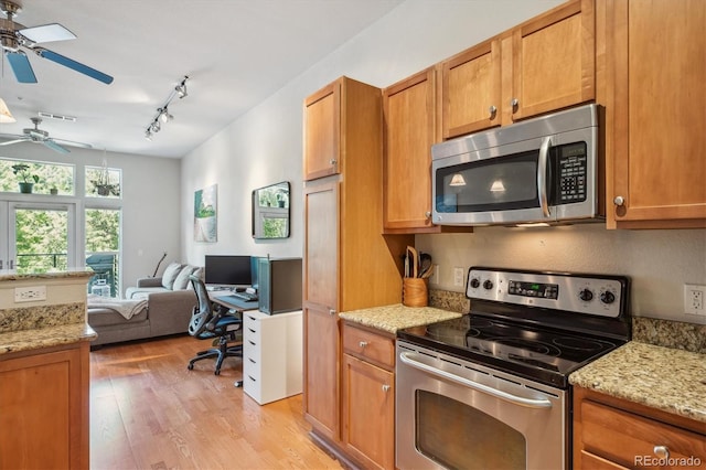 kitchen with appliances with stainless steel finishes, ceiling fan, rail lighting, light stone counters, and light hardwood / wood-style flooring