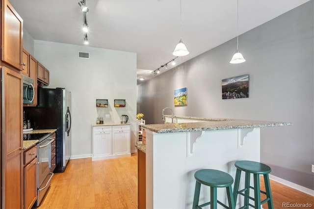 kitchen featuring a breakfast bar, stainless steel appliances, hanging light fixtures, light hardwood / wood-style flooring, and light stone counters