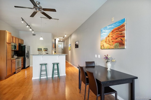 kitchen with a breakfast bar, hanging light fixtures, light wood-type flooring, stainless steel appliances, and light stone counters