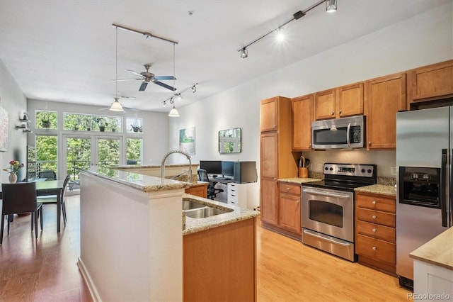 kitchen featuring a center island with sink, sink, light hardwood / wood-style flooring, appliances with stainless steel finishes, and light stone counters