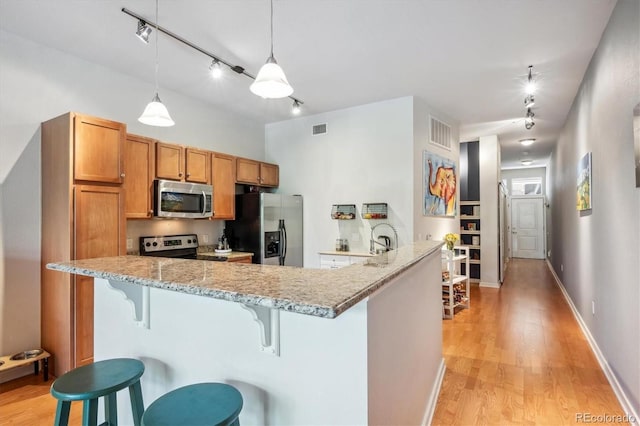 kitchen featuring appliances with stainless steel finishes, decorative light fixtures, a kitchen breakfast bar, light wood-type flooring, and light stone countertops