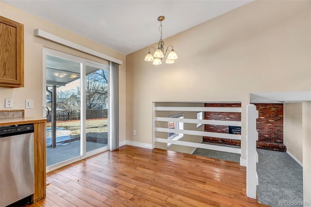 unfurnished dining area featuring an inviting chandelier, lofted ceiling, a fireplace, and light hardwood / wood-style flooring