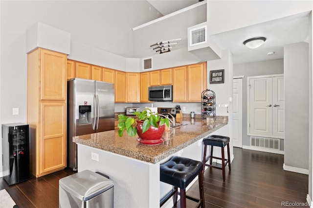 kitchen featuring appliances with stainless steel finishes, light brown cabinets, a kitchen bar, and kitchen peninsula