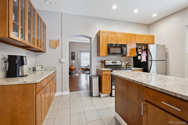 3429 N Adams St, Denver, CO 80205 - kitchen featuring appliances with stainless steel finishes, arched walkways, light stone counters, glass insert cabinets, and brown cabinetry