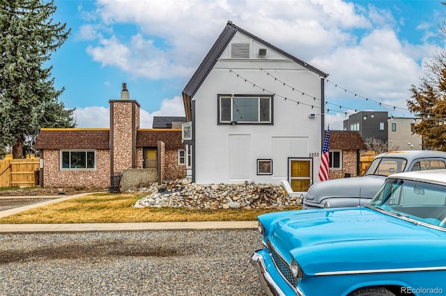 view of front facade with a chimney, fence, and stucco siding