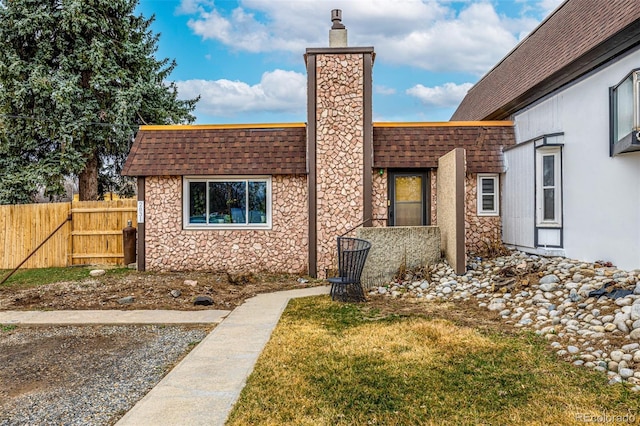 exterior space with roof with shingles, a chimney, a lawn, fence, and stone siding