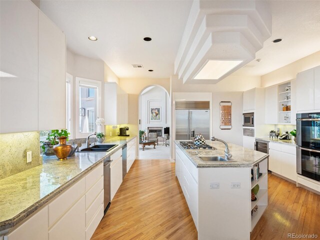 kitchen with built in appliances, sink, an island with sink, white cabinetry, and light hardwood / wood-style flooring