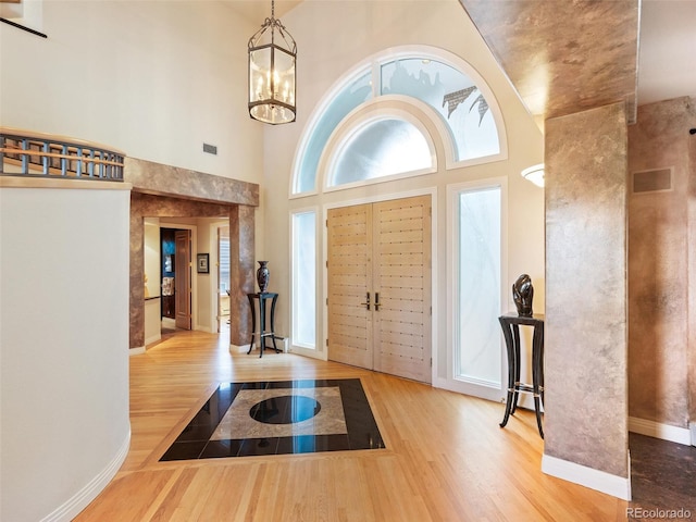 entrance foyer with a notable chandelier, wood finished floors, a towering ceiling, baseboards, and visible vents