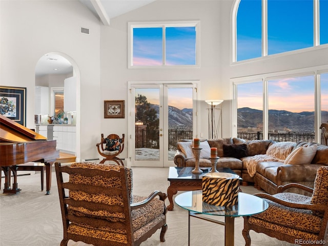 carpeted living room featuring arched walkways, french doors, visible vents, a baseboard heating unit, and a mountain view