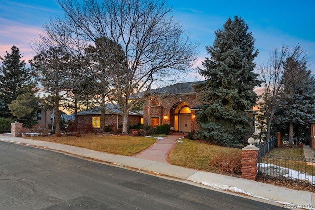 view of front of house with brick siding, fence, and a yard