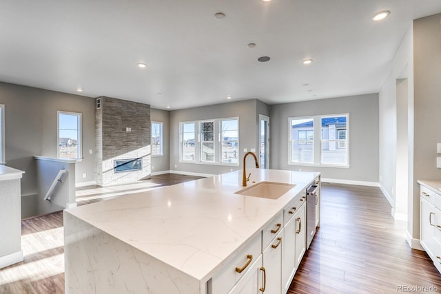 kitchen with white cabinets, an island with sink, light stone countertops, sink, and stainless steel dishwasher