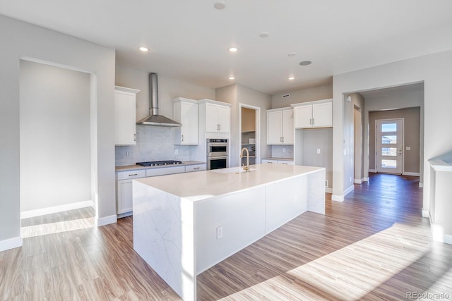 kitchen with white cabinets, gas cooktop, wall chimney range hood, and a kitchen island with sink