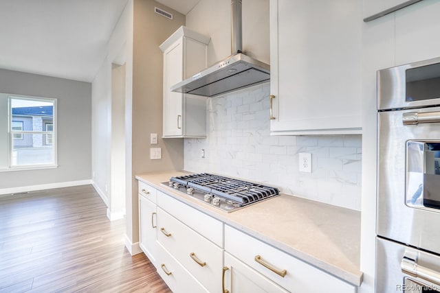 kitchen featuring white cabinetry, wall chimney exhaust hood, hardwood / wood-style floors, decorative backsplash, and appliances with stainless steel finishes