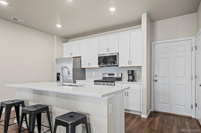 kitchen with a center island with sink, visible vents, stainless steel appliances, dark wood-type flooring, and a kitchen bar