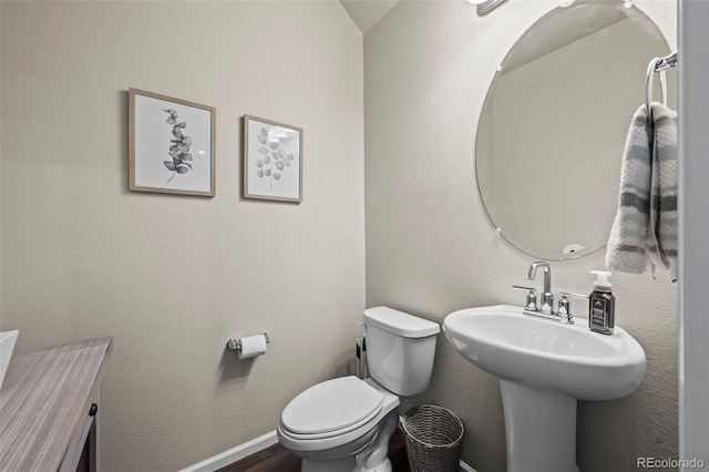 half bathroom with a textured wall, toilet, baseboards, and wood finished floors