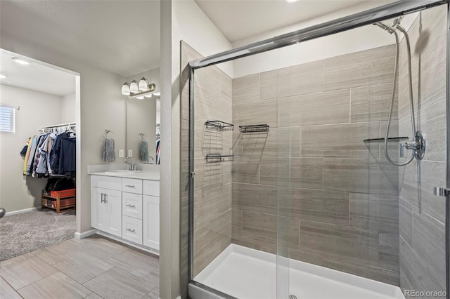 full bath with vanity, a shower stall, a walk in closet, and baseboards