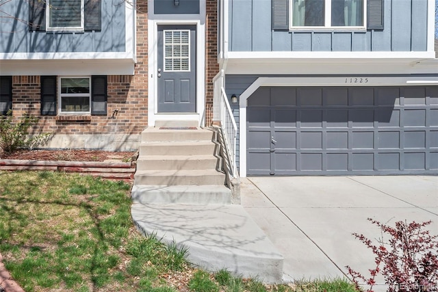 entrance to property with brick siding, driveway, board and batten siding, and an attached garage