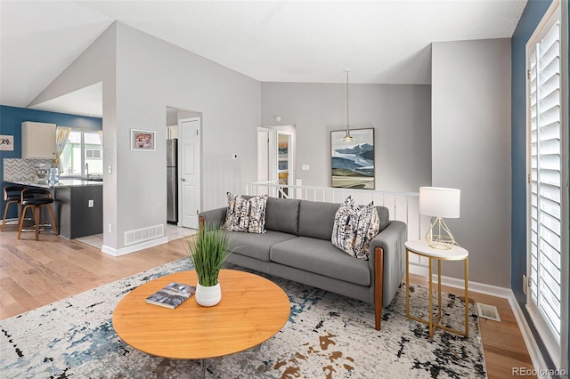living room featuring light wood finished floors, baseboards, vaulted ceiling, and visible vents