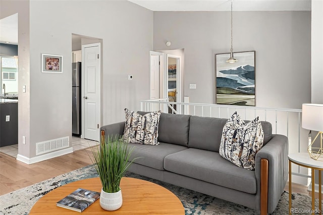 living area featuring high vaulted ceiling, visible vents, baseboards, and light wood-style flooring