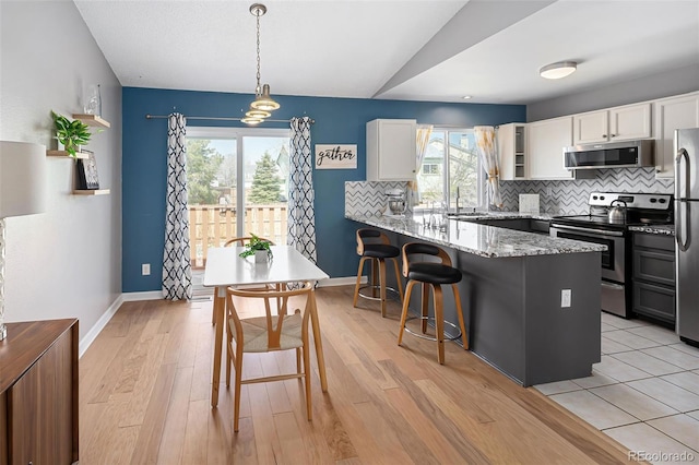 kitchen featuring white cabinets, a kitchen breakfast bar, a peninsula, stainless steel appliances, and light stone counters