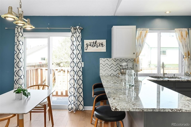 kitchen with baseboards, light wood-type flooring, light stone counters, white cabinets, and a sink