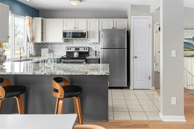 kitchen with a kitchen breakfast bar, light stone counters, white cabinets, stainless steel appliances, and a sink