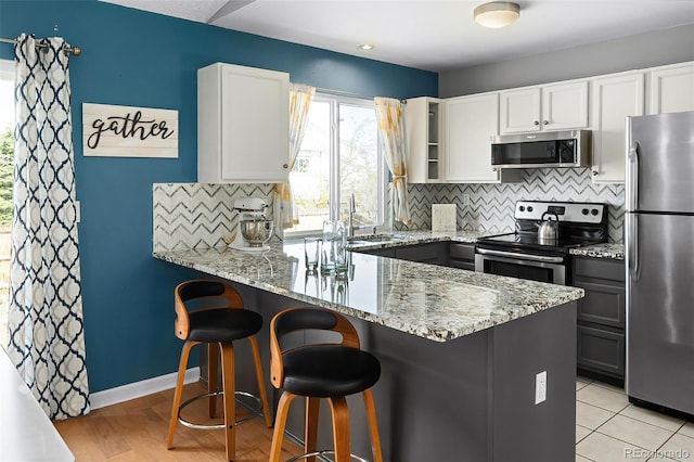 kitchen with tasteful backsplash, a peninsula, light stone counters, and stainless steel appliances