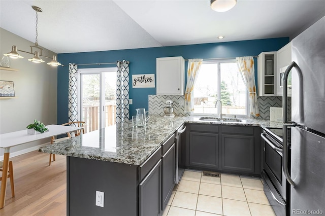 kitchen with light stone countertops, tasteful backsplash, a peninsula, a sink, and stainless steel appliances