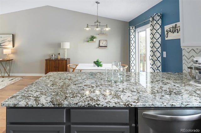 kitchen with light stone countertops, light wood-style flooring, dishwasher, lofted ceiling, and decorative backsplash