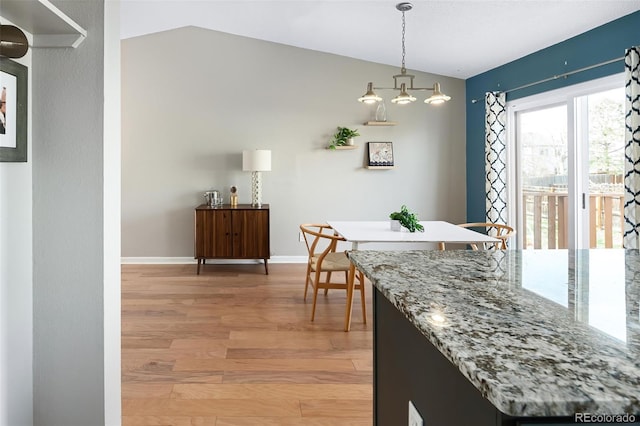 dining space with baseboards, light wood finished floors, and vaulted ceiling