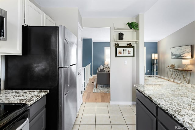 kitchen with white cabinets, baseboards, stainless steel appliances, light stone countertops, and light tile patterned flooring