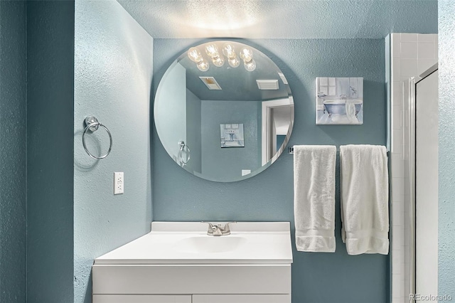 full bathroom featuring an enclosed shower, a textured wall, vanity, and visible vents