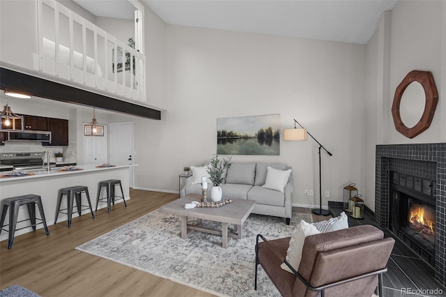 living room featuring light wood-style floors, a tiled fireplace, a high ceiling, and baseboards