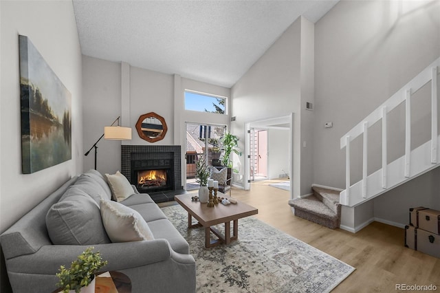 living area with high vaulted ceiling, wood finished floors, a tiled fireplace, stairway, and baseboards