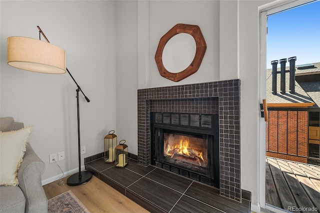 detailed view of a tiled fireplace, wood finished floors, and baseboards