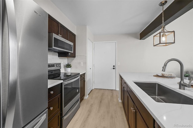 kitchen featuring stainless steel appliances, a sink, light wood-style flooring, hanging light fixtures, and dark brown cabinetry