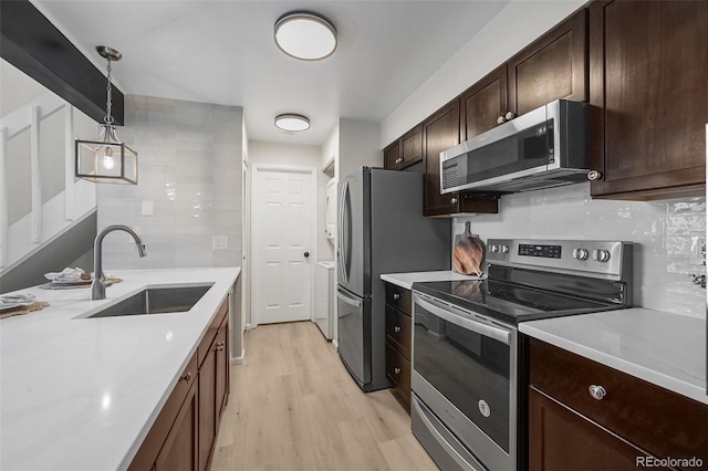 kitchen with appliances with stainless steel finishes, a sink, light wood-style floors, and tasteful backsplash