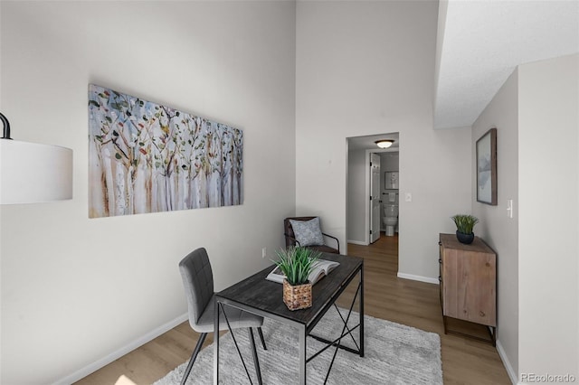 dining area with wood finished floors, baseboards, and a towering ceiling