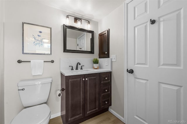 bathroom featuring baseboards, toilet, wood finished floors, and vanity