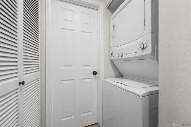 laundry area featuring stacked washer and clothes dryer, a heating unit, and a textured wall