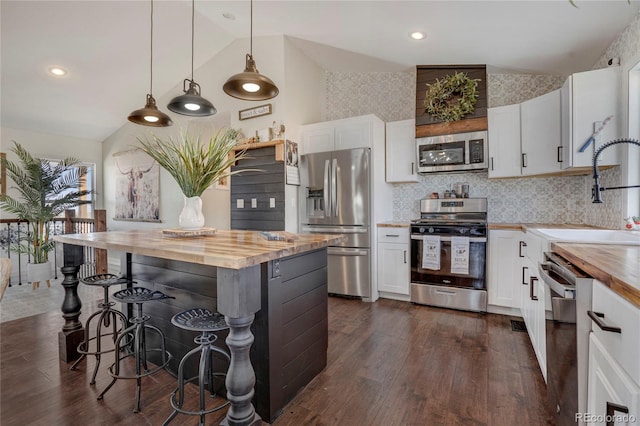 kitchen featuring vaulted ceiling, butcher block countertops, a sink, dark wood finished floors, and appliances with stainless steel finishes