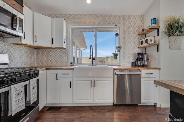 kitchen with white cabinets, stainless steel appliances, a sink, butcher block countertops, and wallpapered walls
