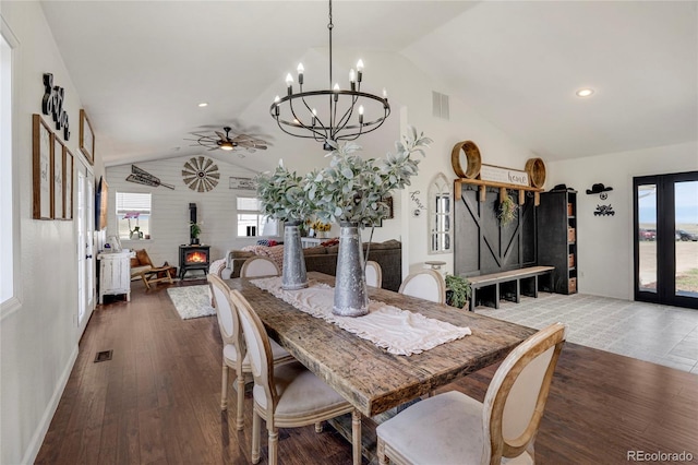 dining area featuring lofted ceiling, wood finished floors, a wood stove, and ceiling fan with notable chandelier