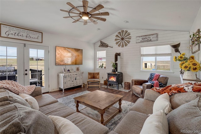 living area featuring vaulted ceiling, a ceiling fan, wooden walls, a wood stove, and french doors