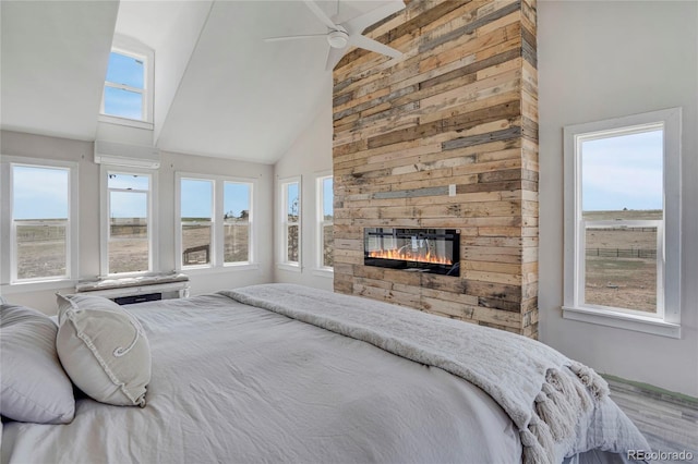 bedroom with wood finished floors, a fireplace, high vaulted ceiling, and multiple windows