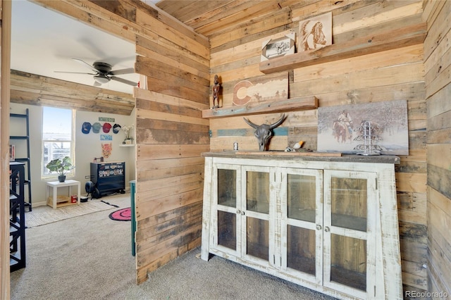 interior space featuring carpet flooring, wooden walls, baseboards, ceiling fan, and wooden ceiling