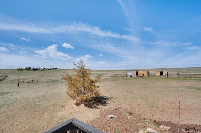 view of yard featuring fence, a rural view, an outdoor structure, and an exterior structure