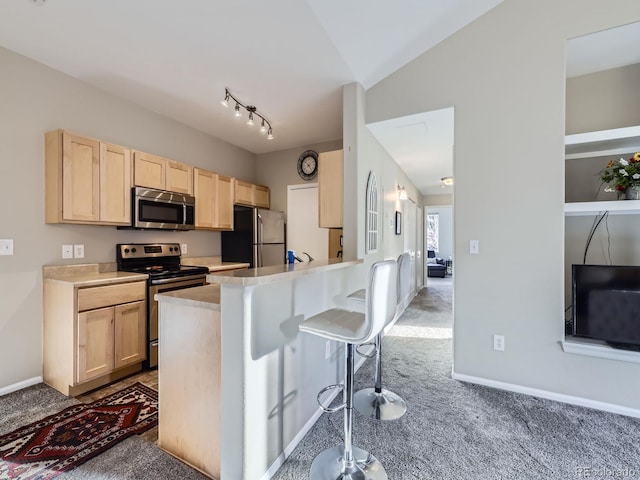 kitchen featuring lofted ceiling, a breakfast bar, stainless steel appliances, carpet flooring, and light brown cabinetry